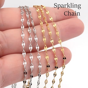 Peut inclure: Gros plan sur plusieurs chaînes délicates en argent et en or. Les chaînes présentent un motif répétitif de maillons en forme de losange. Le texte "Sparkling Chain" est visible dans le coin supérieur droit.