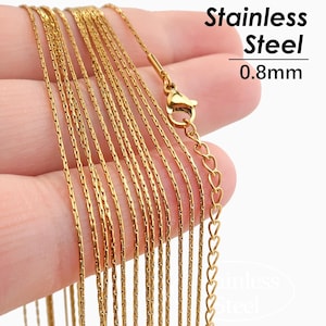 Könnte beinhalten: Nahaufnahme einer goldfarbenen Edelstahl-Halskette. Die Kette ist 0,8 mm dick und hat ein filigranes Design. Der Verschluss und die Verlängerungskette sind sichtbar, mit herzförmigen Gliedern. Der Text lautet "Stainless Steel 0.8mm".