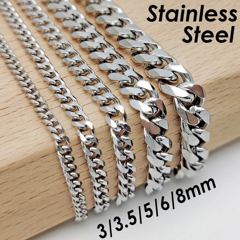 Op de afbeelding: Een verzameling roestvrijstalen gourmettekettingen in verschillende breedtes, vari&euml;rend van 3 mm tot 8 mm, gepresenteerd op een houten blok. De zilverkleurige kettingen reflecteren het licht, wat hun gepolijste afwerking benadrukt. De tekst "Stainless Steel" en de maten zijn zichtbaar.