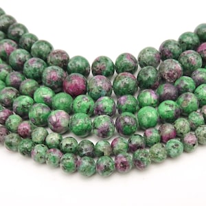 Puede incluir: Una hebra de cuentas de piedras preciosas verdes y rosas. Las cuentas son redondas y tienen un aspecto moteado.