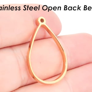 以下が含まれることがあります： ジュエリー作りのための、ゴールドトーンのステンレススチール製オープンバックベゼルペンダント。ベゼルは、上部に小さな穴のある涙の形をしています。