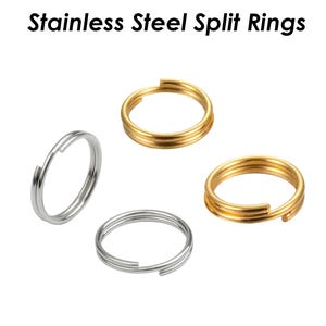 Pode incluir: Quatro anéis partidos de aço inoxidável, dois dourados e dois prateados. Os anéis são todos do mesmo tamanho e estão dispostos em um padrão simétrico.