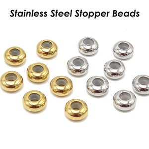 May include: A collection of 12 stainless steel stopper beads, 6 gold and 6 silver, with a clear centre hole. The beads are round and have a smooth, shiny finish.