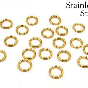 May include: A collection of 18 gold-colored jump rings made of stainless steel. The rings are all the same size and are arranged in a scattered pattern on a white background.