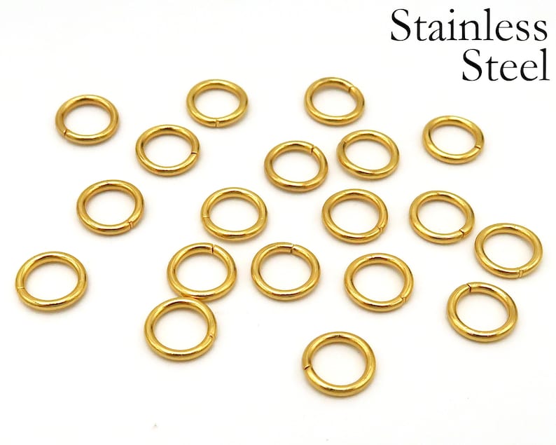 May include: A collection of 18 gold-colored jump rings made of stainless steel. The rings are all the same size and are arranged in a scattered pattern on a white background.