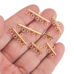 May include: Eight gold-toned metal connector clasps for jewelry making. Each clasp has four loops for attaching chains or cords.
