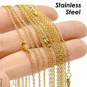 May include: A close-up of a gold-toned stainless steel chain necklace. The chain is made of multiple strands of thin, linked metal. The chain is displayed on a hand, with the text "Stainless Steel" visible in the background.