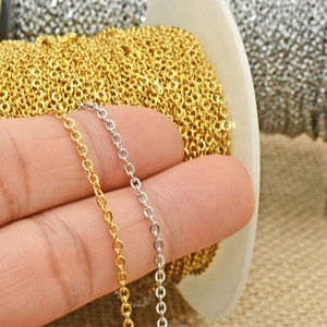 May include: Two spools of chain, one gold and one silver, are shown. A hand is holding a strand of each chain.