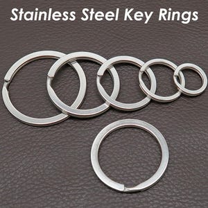 Könnte beinhalten: Edelstahl-Schlüsselringe in verschiedenen Größen, angeordnet auf einem braunen Hintergrund. Die Ringe sind silberfarben und aus Metall gefertigt. Der Text "Stainless Steel Key Rings" ist oben im Bild zu sehen.