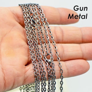 Op de afbeelding: Meerdere strengen van een ketting van donkergrijs metaal, een soort sieradenketting, zijn te zien in een close-up afbeelding. De ketting wordt in een hand gehouden, en de afbeelding is gemaakt vanuit een licht hellend perspectief.