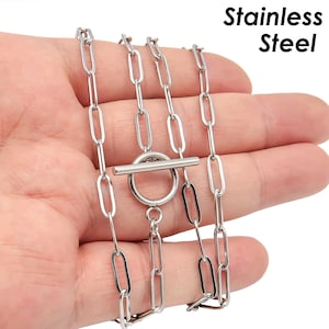 Op de afbeelding: Een zilveren ketting met een schuifgesp. De ketting is gemaakt van meerdere strengen met gekoppelde ovalen. De ketting is gemarkeerd met "RVS".