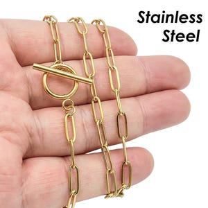 Könnte beinhalten: Eine goldfarbene Halskette aus Edelstahl mit einem Toggle-Verschluss. Die Kette besteht aus miteinander verbundenen ovalen Gliedern.