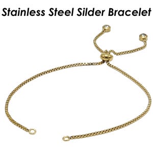 Könnte beinhalten: Ein goldfarbenes Armband aus Edelstahl mit Schieber und zwei kleinen, klaren Steinen an den Enden.