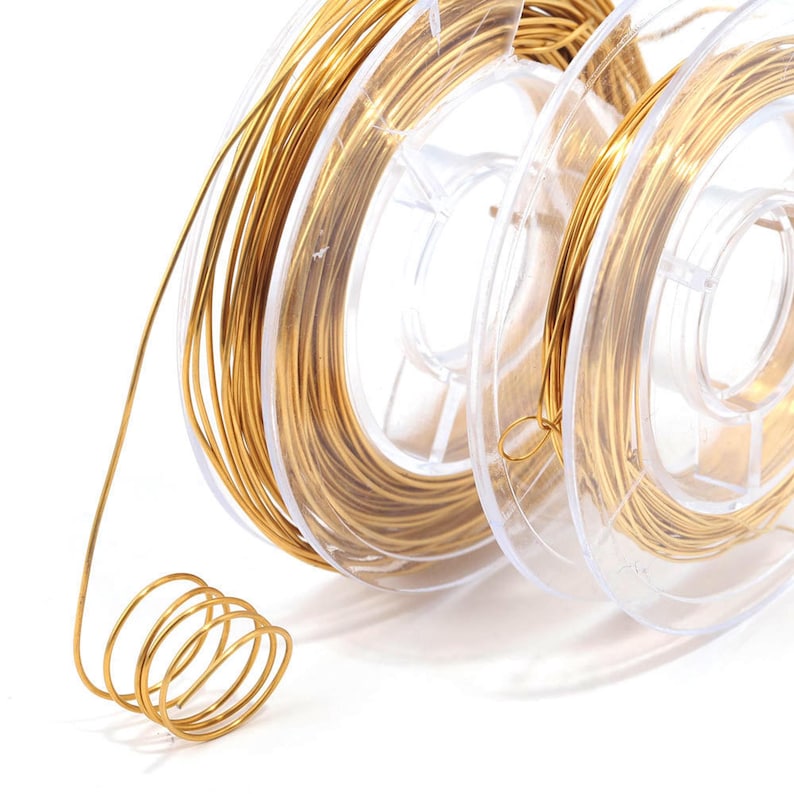May include: A spool of gold-colored wire on a clear plastic spool. The wire is wound tightly around the spool and is ready to be used for crafting projects.