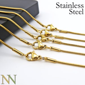 May include: Five gold-toned stainless steel snake chains with lobster claw clasps. The chains are arranged in a staggered pattern, with the longest chain at the top and the shortest chain at the bottom.