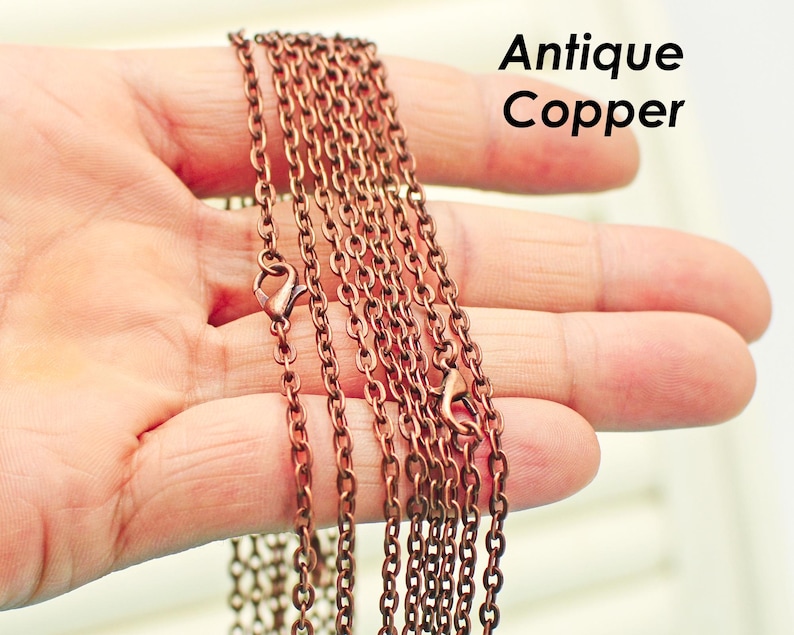 May include: Antique copper chain necklace with multiple strands of chain. The chain is held in a hand.