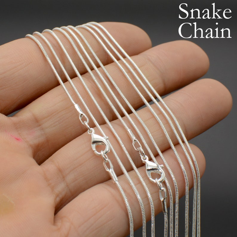 May include: A set of silver snake chains of varying lengths. The chains are laid out on a hand, showing the different sizes and styles.