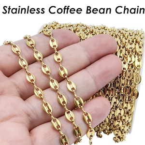 Könnte beinhalten: Eine goldfarbene Edelstahlkette in Form von Kaffeebohnen. Die Kette besteht aus kleinen, ovalen Gliedern, die an Kaffeebohnen erinnern.