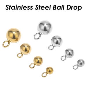 May include: A set of seven stainless steel ball drop charms in gold and silver. The charms are different sizes and have a loop at the top for attaching to jewellery.