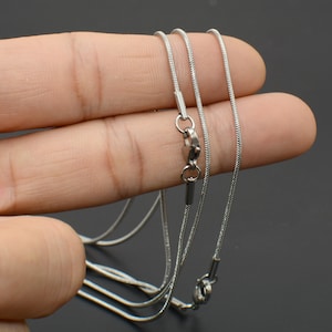 May include: Three silver snake chains of different lengths, lying on a finger.