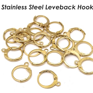 May include: A close-up of a pile of gold-toned stainless steel leverback earring hooks. The hooks are all the same size and shape, and they are arranged in a random pattern.