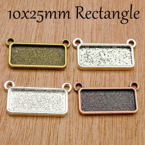 Könnte beinhalten: Vier rechteckige Metall-Anhängerfassungen in 10x25mm, jede mit zwei kleinen Ösen an den oberen Ecken. Das Set enthält eine antike Bronze-, Silber-, helle Silber- und Kupferausführung, alle mit texturierten Innenflächen.