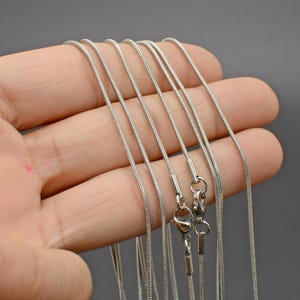 May include: A set of silver snake chains of varying lengths. The chains are made of stainless steel and have a smooth, polished finish.