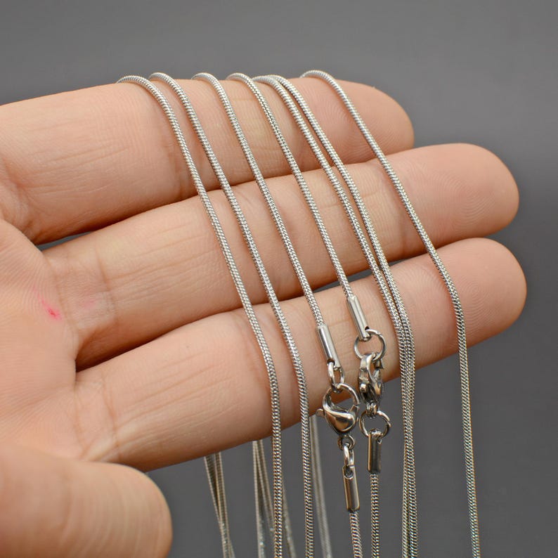 May include: A set of silver snake chains of varying lengths. The chains are made of stainless steel and have a smooth, polished finish.
