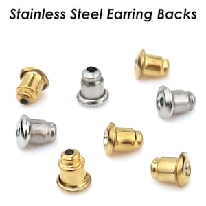 Puede incluir: Una variedad de cierres de pendientes de acero inoxidable en tonos dorados y plateados. La imagen muestra varios cierres de pendientes, con el texto "Stainless Steel Earring Backs" en la parte superior. Los cierres son de varias formas y tamaños.