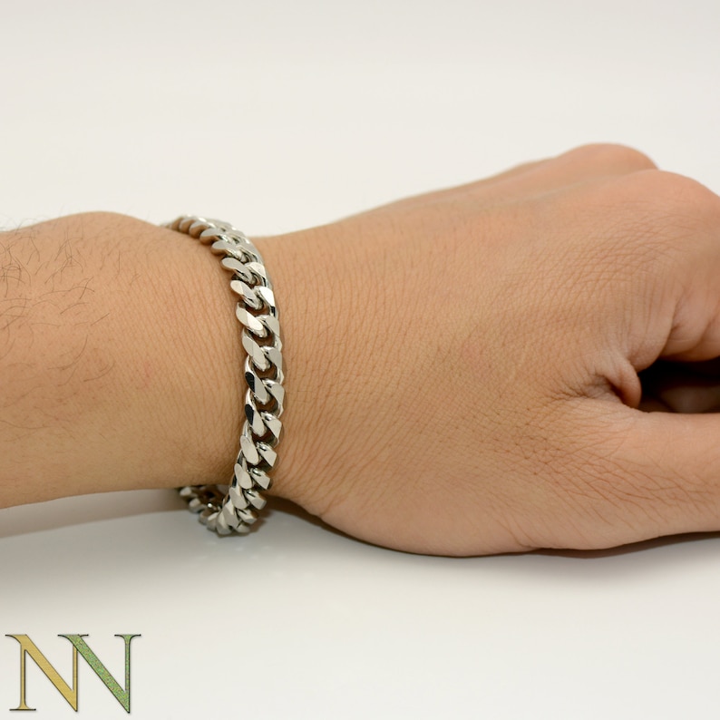 Op de afbeelding: Een zilveren gourmet armband wordt om een pols gedragen. De armband is gemaakt van in elkaar grijpende schakels, wat een gedurfd en klassiek ontwerp cre&euml;ert. De armband heeft een heldere, glanzende zilveren kleur.