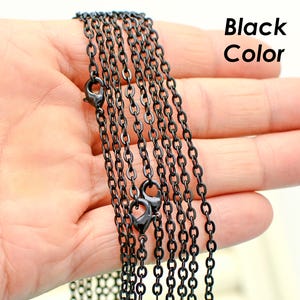 May include: Multiple strands of black chain, likely for jewelry making, are shown in a hand. The chain is a simple, linked design.