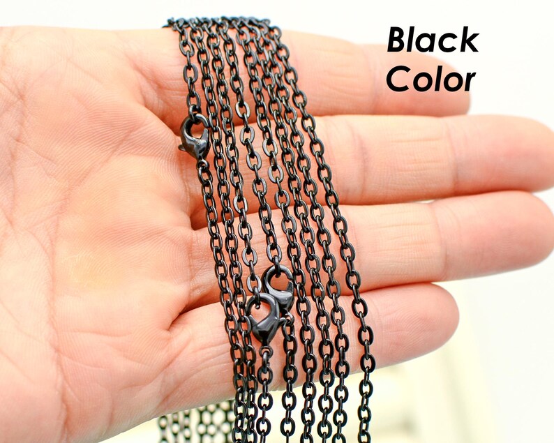 May include: Multiple strands of black chain, likely for jewelry making, are shown in a hand. The chain is a simple, linked design.