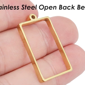 May include: Gold-toned stainless steel open back bezel pendant with a loop at the top. The bezel is rectangular and has a smooth, polished finish.