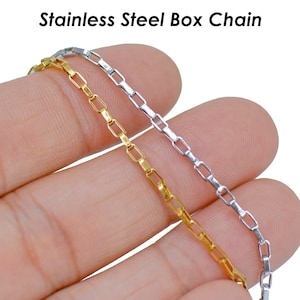 May include: Two stainless steel box chains, one gold and one silver, are shown on a hand.  "Stainless Steel Box Chain" is written in the top center of the image.