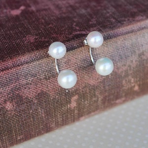 May include: A pair of silver earrings with two white pearls on each earring.