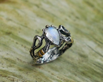 May include: A silver ring with a pear-shaped moonstone set in a twisted branch design. The ring has a gold accent on the band.