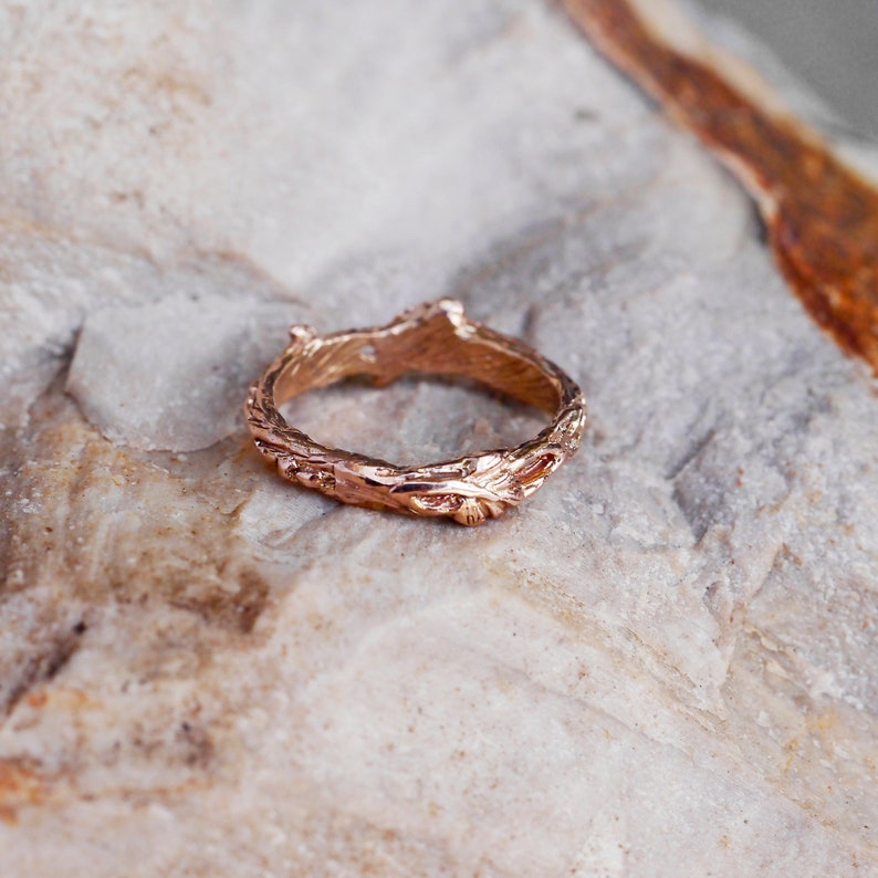 Pu&ograve; includere: Un anello in oro rosa con un design delicato e intricato che ricorda un ramo con foglie. L'anello &egrave; realizzato in metallo e ha una finitura liscia e lucida.