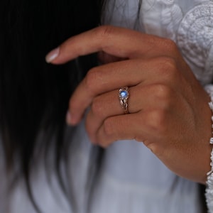 Puede incluir: Un delicado anillo con una piedra de luna azul engastada en una banda de oro rosa. El anillo est&aacute; dise&ntilde;ado de forma intrincada con un patr&oacute;n de espiral.