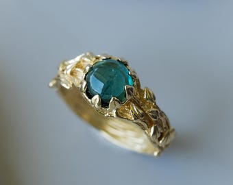 May include: A gold ring with a green gemstone set in a leafy design.