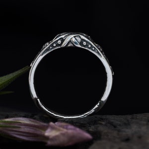 May include: A silver ring with a textured, twisted band and small dots along the edges.