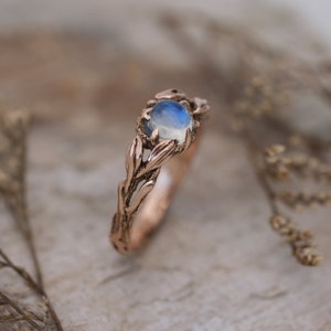 Puede incluir: Un anillo de oro rosa con un delicado dise&ntilde;o de rama y una piedra de luna redonda.