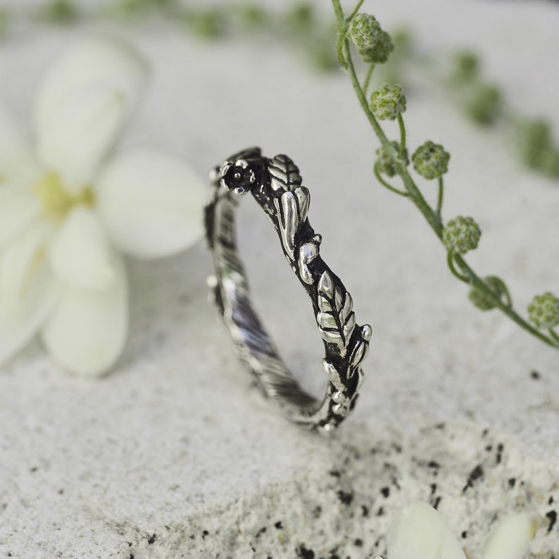 Peut inclure: Une bague argent&eacute;e avec un motif inspir&eacute; de la nature. La bague pr&eacute;sente un motif d&eacute;taill&eacute; de feuilles et de vignes, cr&eacute;ant une esth&eacute;tique d&eacute;licate et organique. La bague est pos&eacute;e sur un fond doux et neutre, mettant en valeur ses d&eacute;tails complexes.