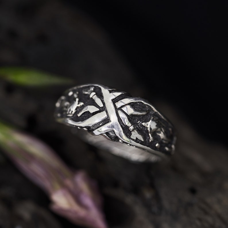 May include: A silver ring with a detailed, textured design. The ring features a cross-shaped pattern with intricate details.