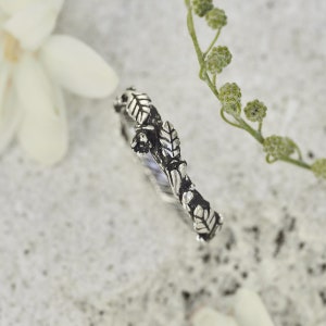 Peut inclure: Une bague en argent avec un motif de feuilles. La bague pr&eacute;sente des motifs d&eacute;taill&eacute;s de feuilles et de branches, cr&eacute;ant une esth&eacute;tique inspir&eacute;e de la nature. La bague est pos&eacute;e sur un fond neutre, soulignant son design complexe. Un bijou d&eacute;licat.