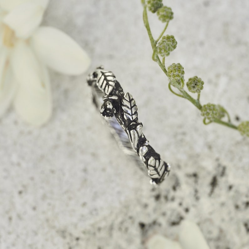 Peut inclure: Une bague en argent avec un motif de feuilles. La bague pr&eacute;sente des motifs d&eacute;taill&eacute;s de feuilles et de branches, cr&eacute;ant une esth&eacute;tique inspir&eacute;e de la nature. La bague est pos&eacute;e sur un fond neutre, soulignant son design complexe. Un bijou d&eacute;licat.