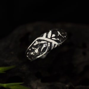 May include: A silver ring with an intricate design of interwoven branches and leaves.