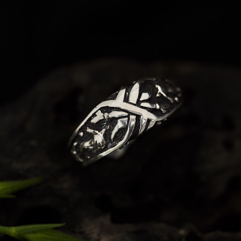 May include: A silver ring with an intricate design of interwoven branches and leaves.