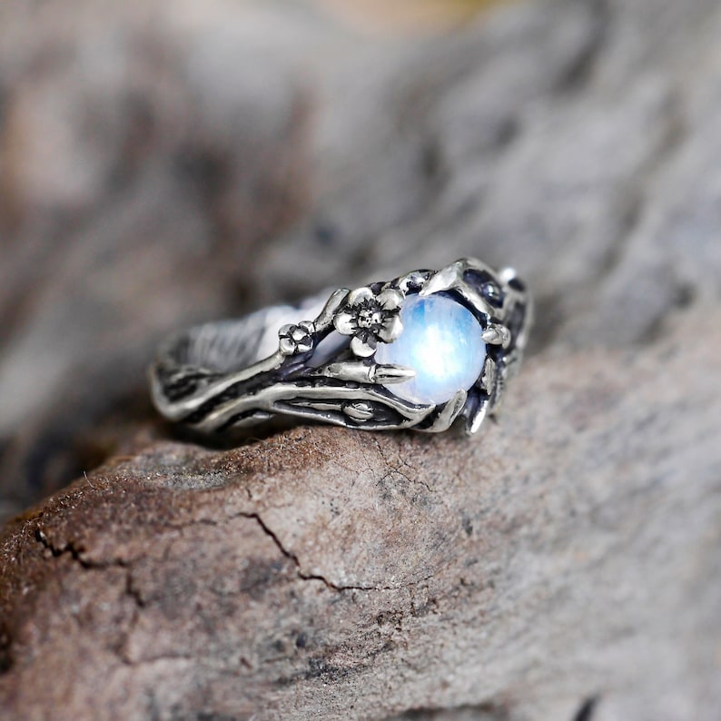 May include: A silver ring with a moonstone set in a delicate branch design. The ring features small flower accents.