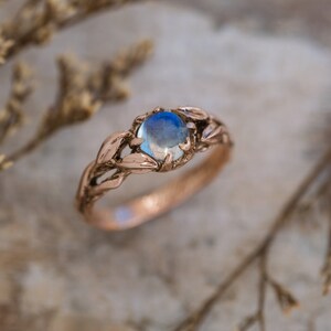 Puede incluir: Un delicado anillo de oro rosa con una piedra de luna azul engastada en un dise&ntilde;o de hojas.