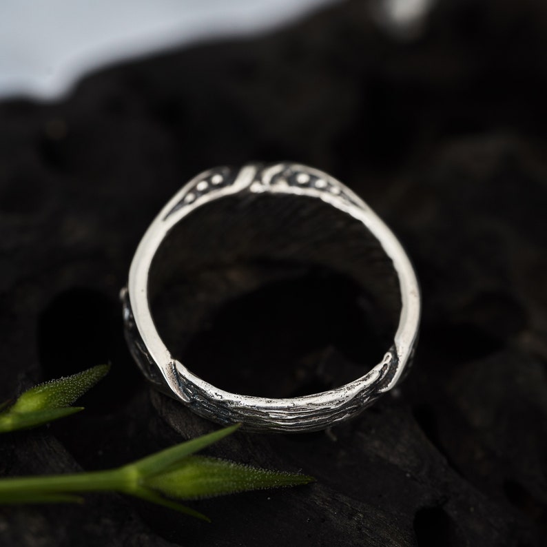 May include: A silver ring with a detailed, textured design. The ring is made of a smooth, polished metal and has a circular shape.